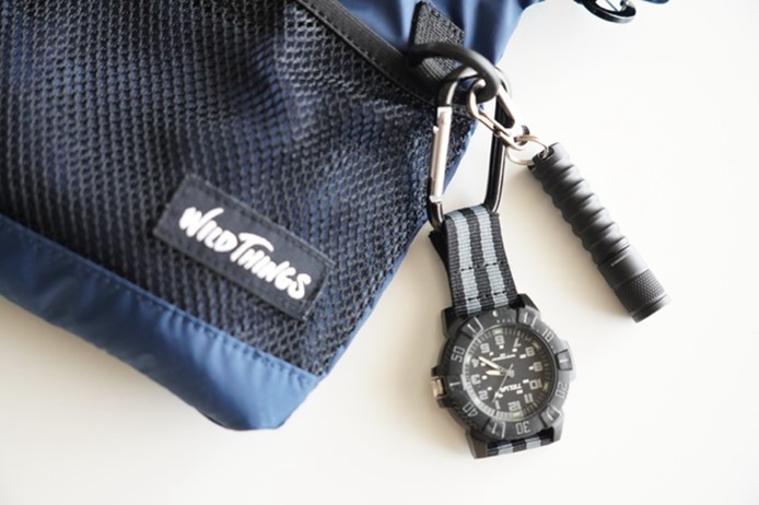 写真：小学生用の防災ポーチに吊り下げタイプの時計とミニライトがついている